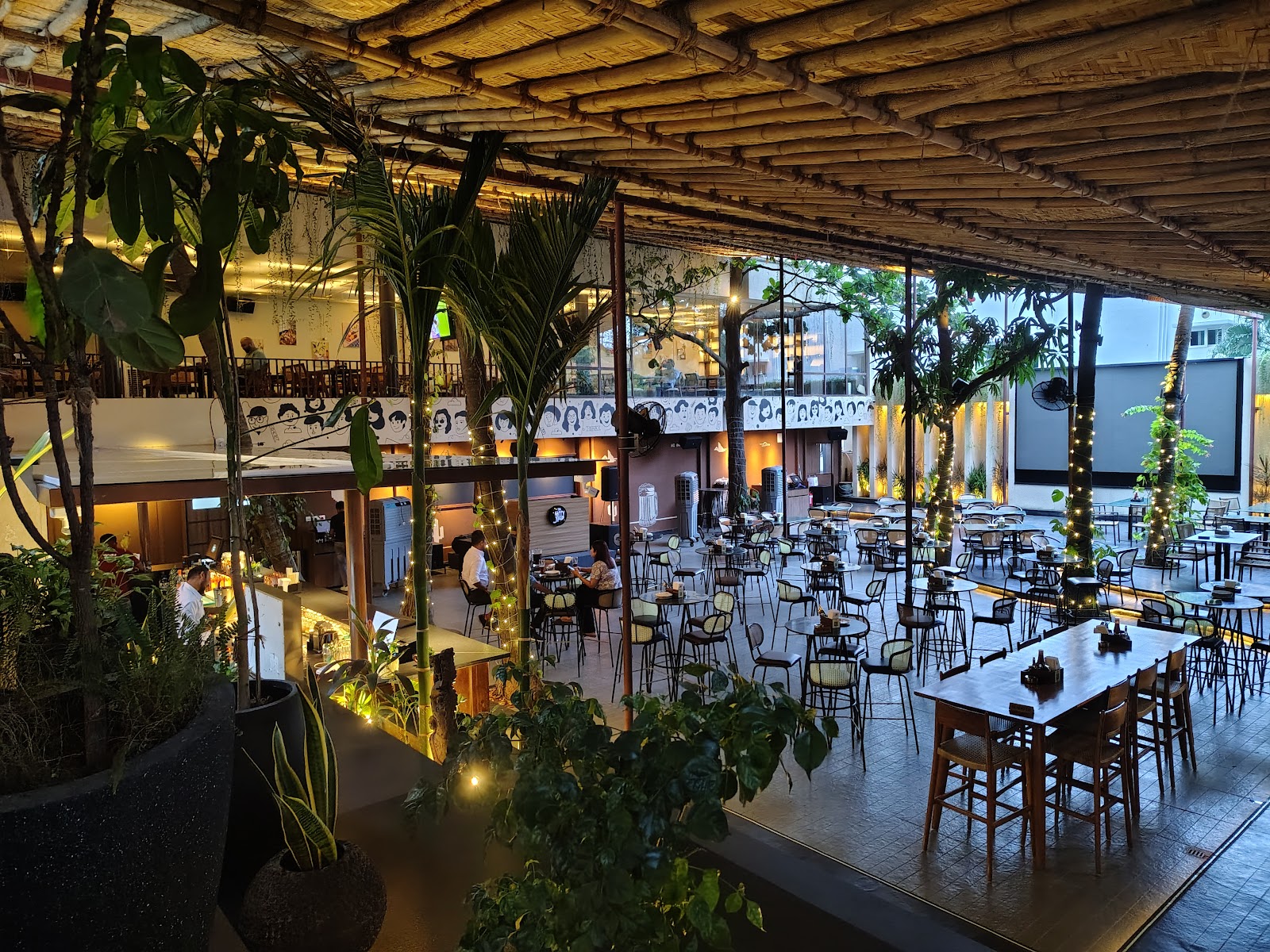 Bar stools and high tables under a slatted canopy along the edge of the yard.