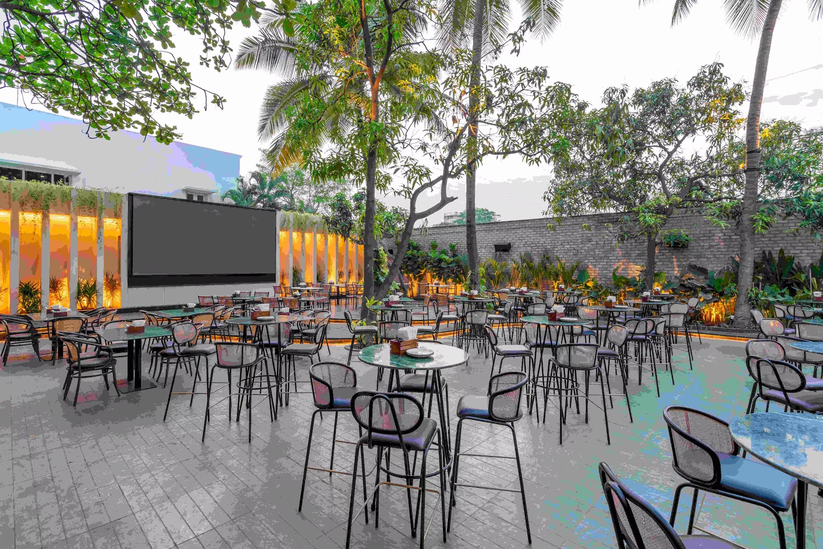 Round tables facing the outdoor projection screen, palms behind it.