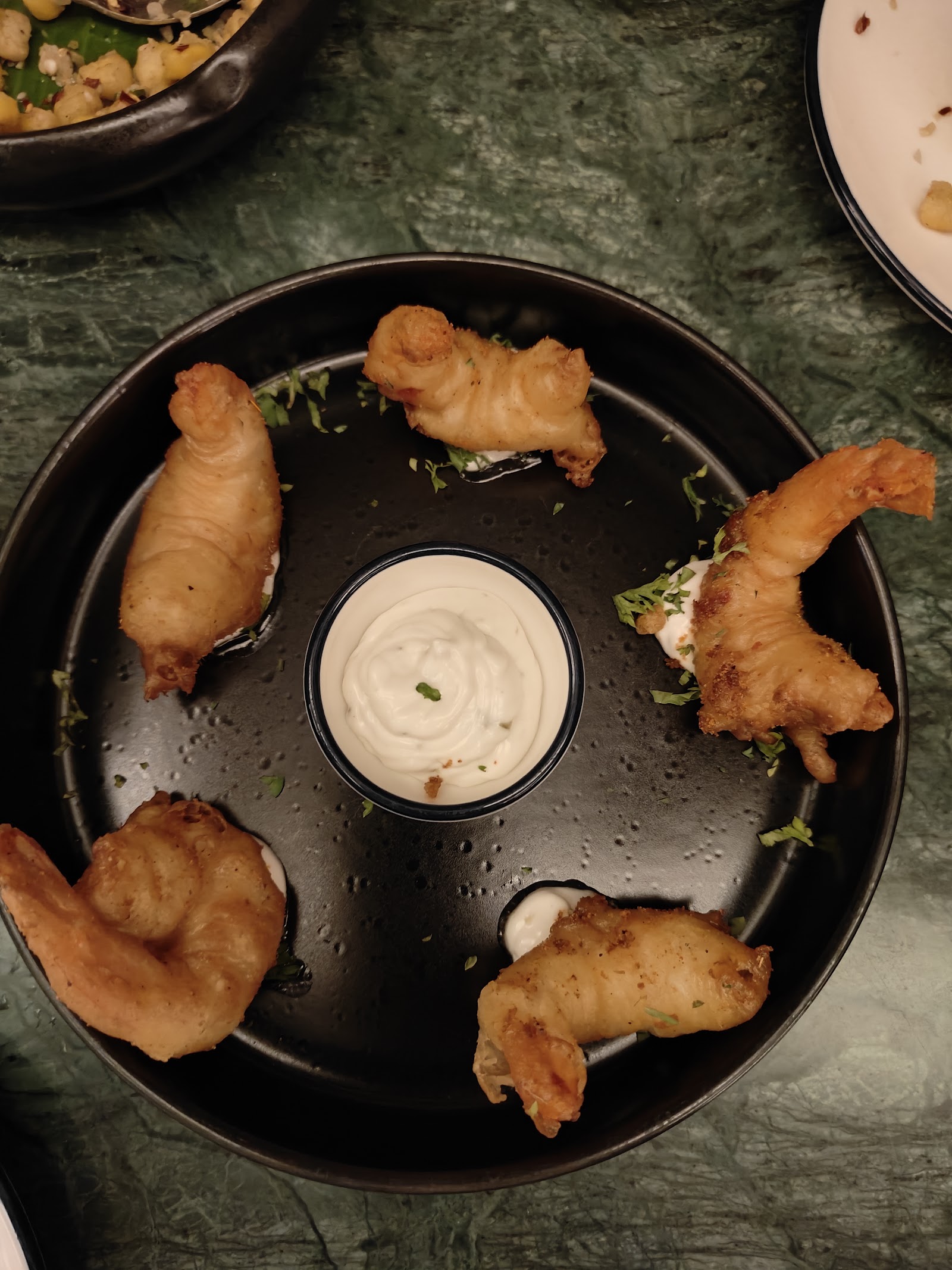 Battered prawns ringed around a dip on a dark plate.