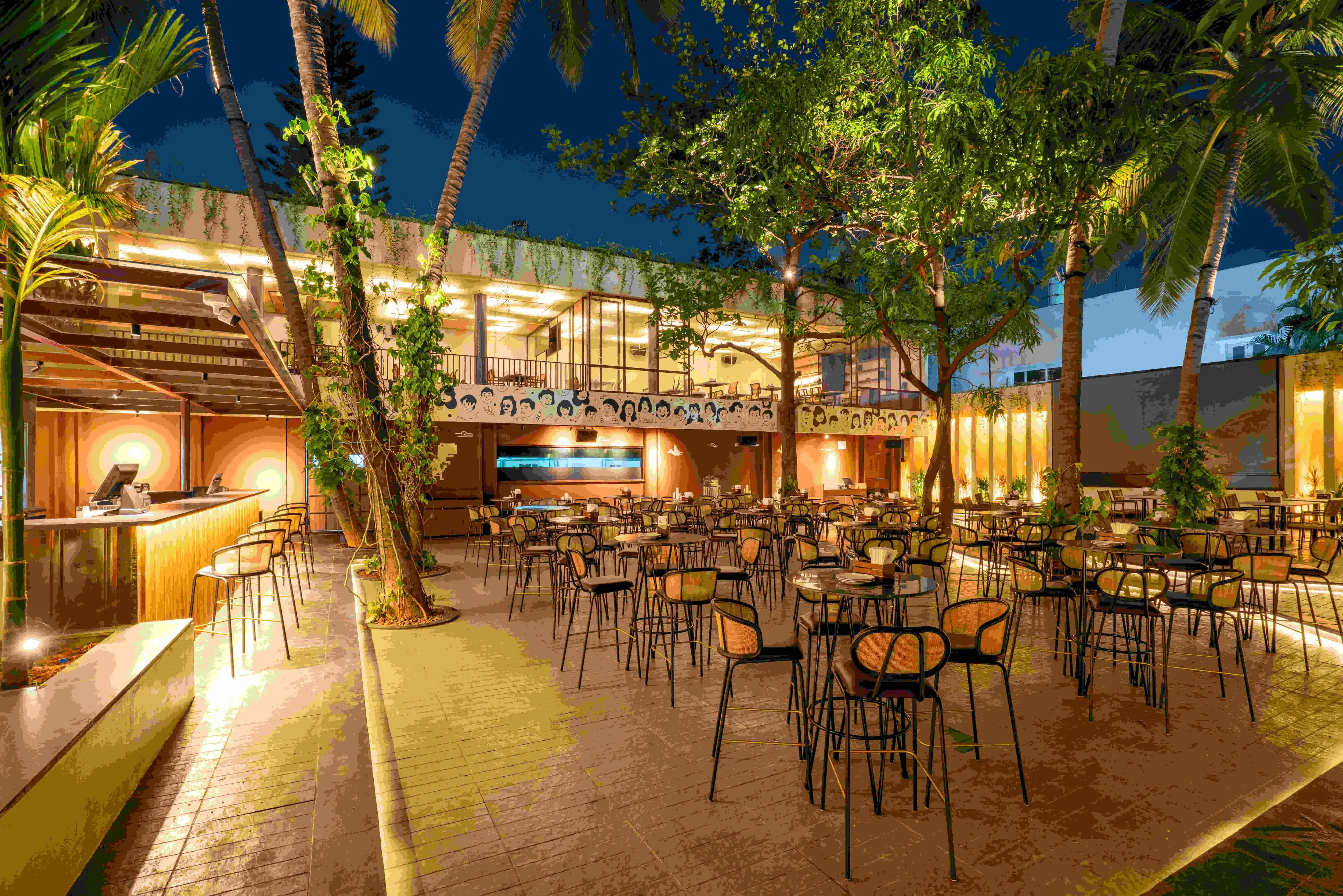 Warm light along the bar side of the yard, palms above the seating.