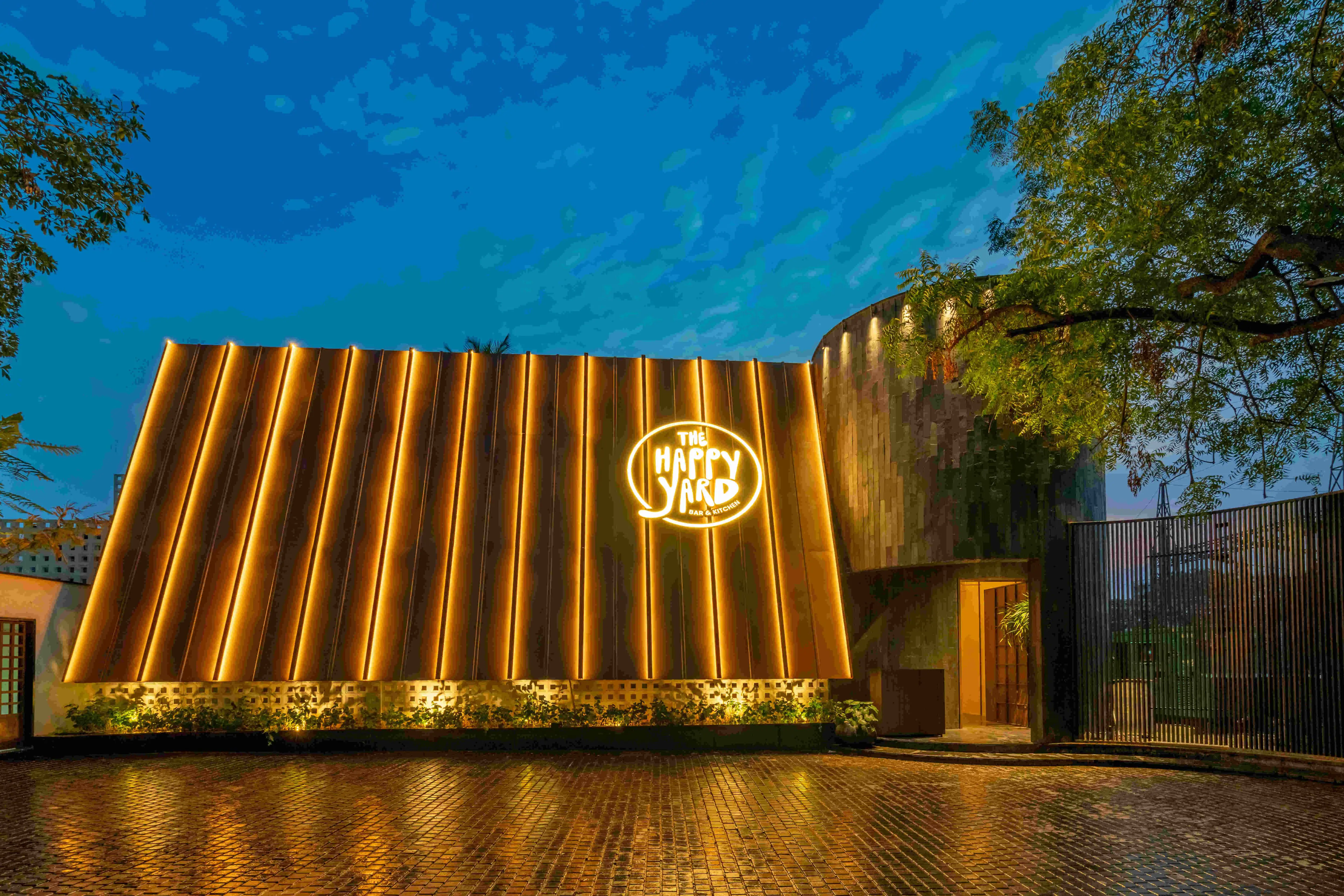 The slatted wall at dusk with the logo lit, seen from the approach.