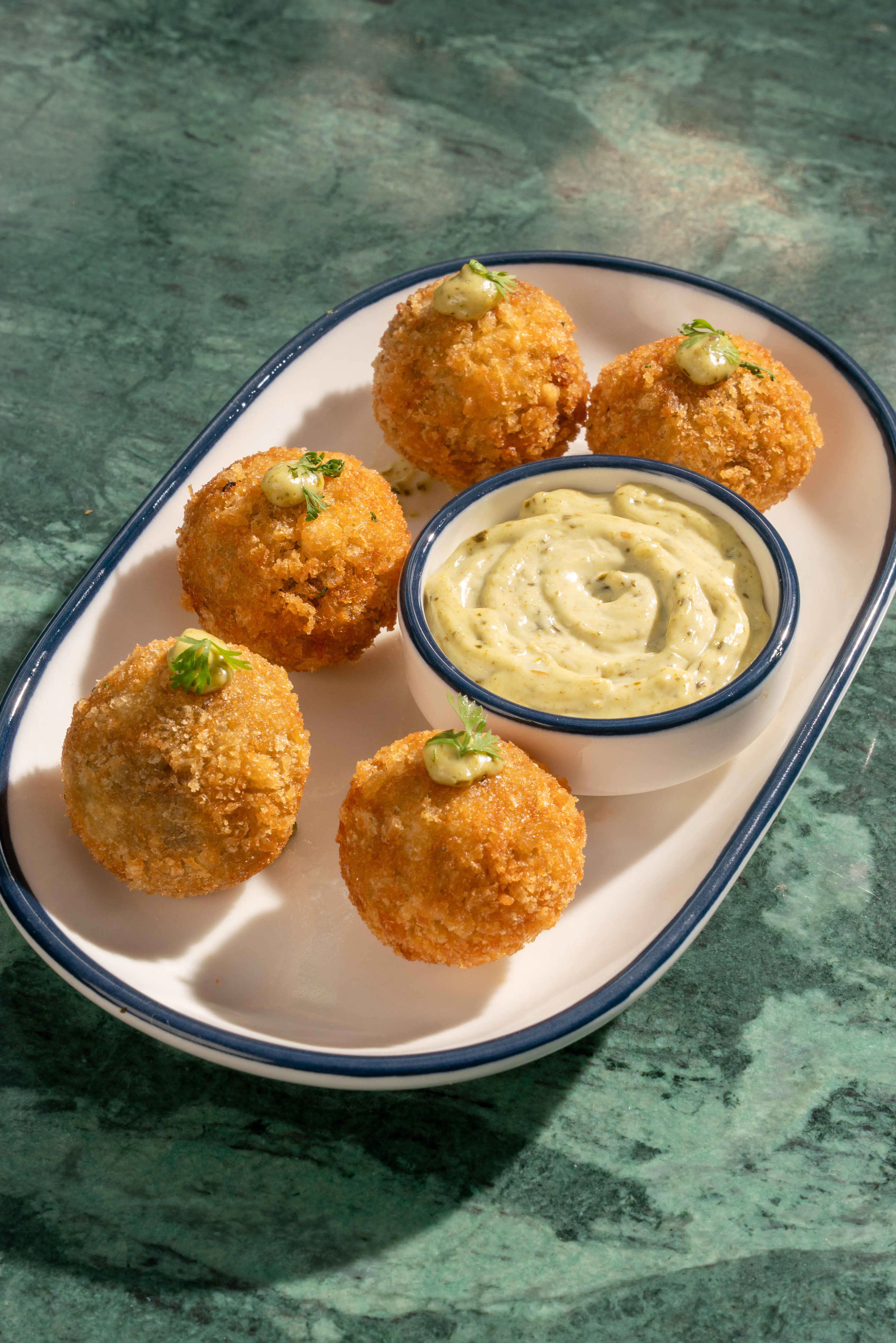 Four crumbed arancini with a dip on an oval plate.