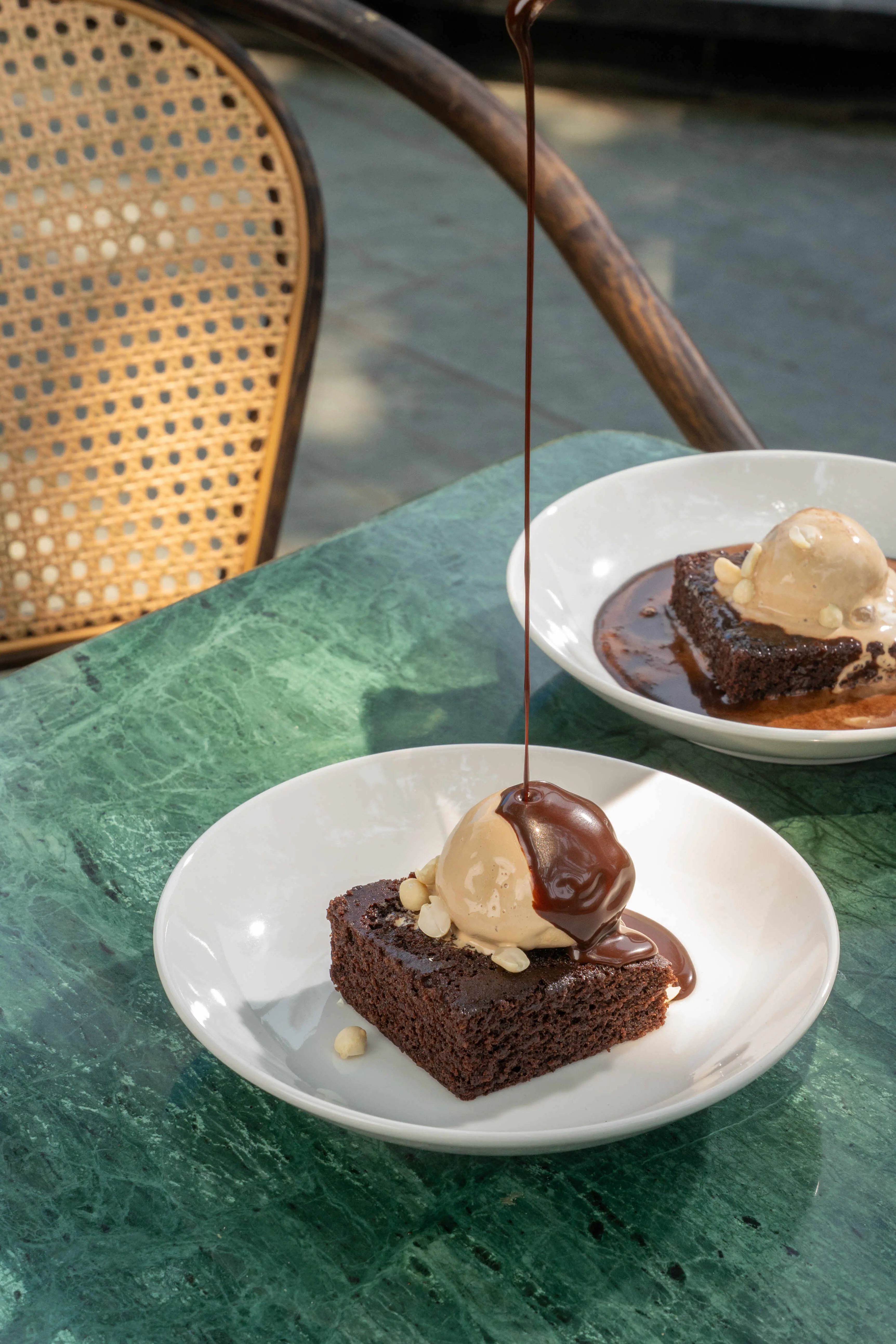Sauce poured over a brownie with ice cream, a second plate behind.