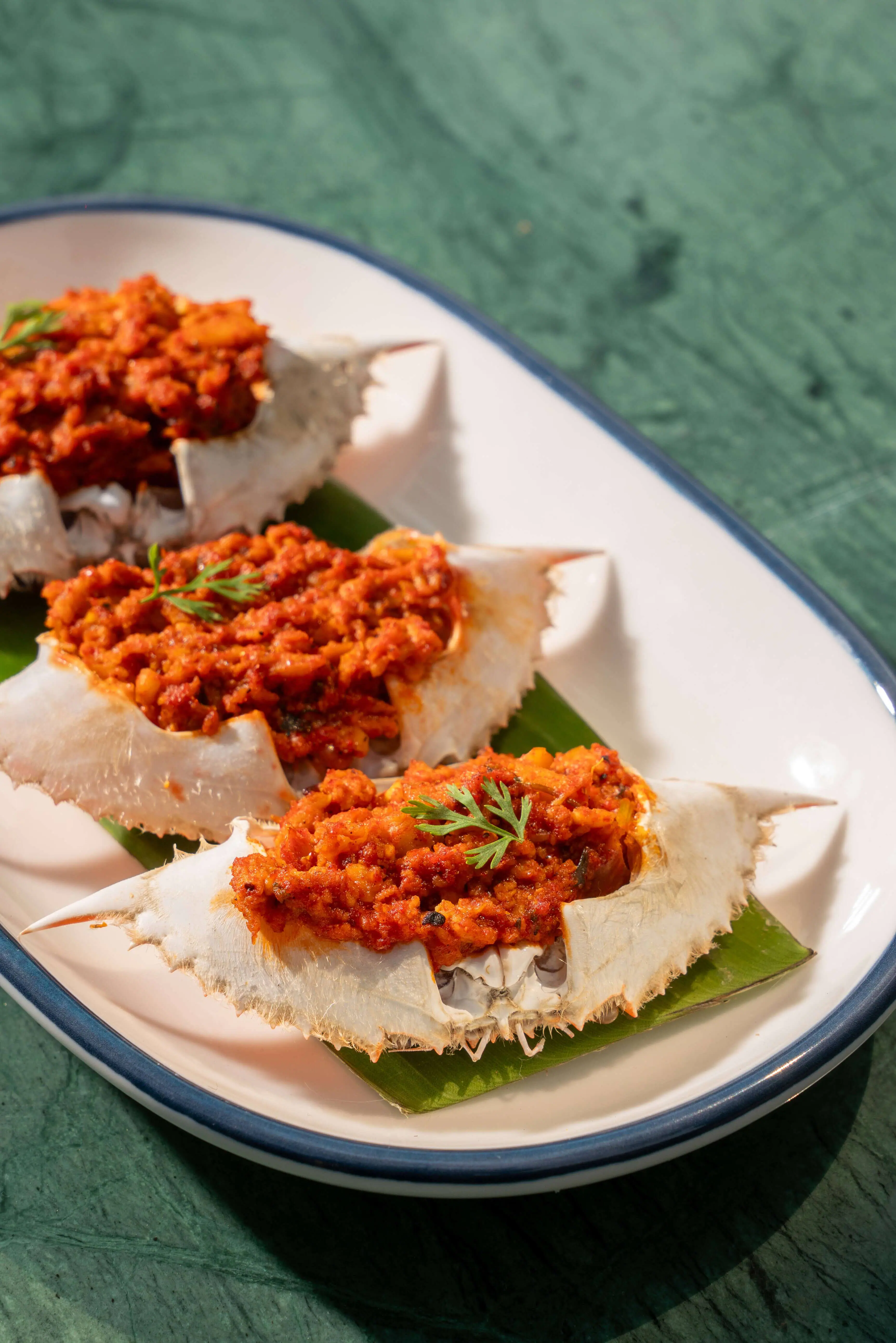 Crab shells filled with a red masala on a banana leaf.