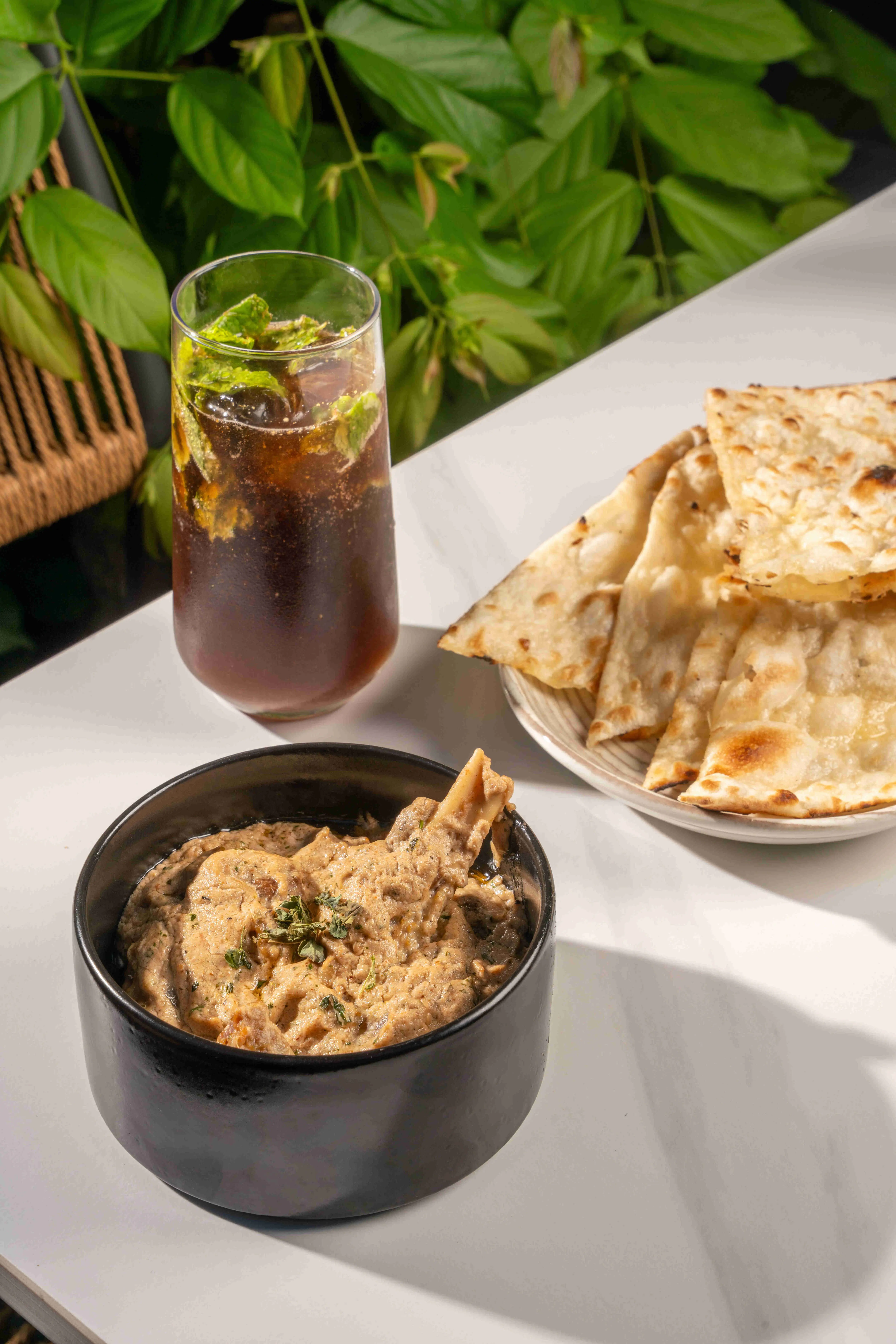 A dark bowl of curry with naan and an iced drink.