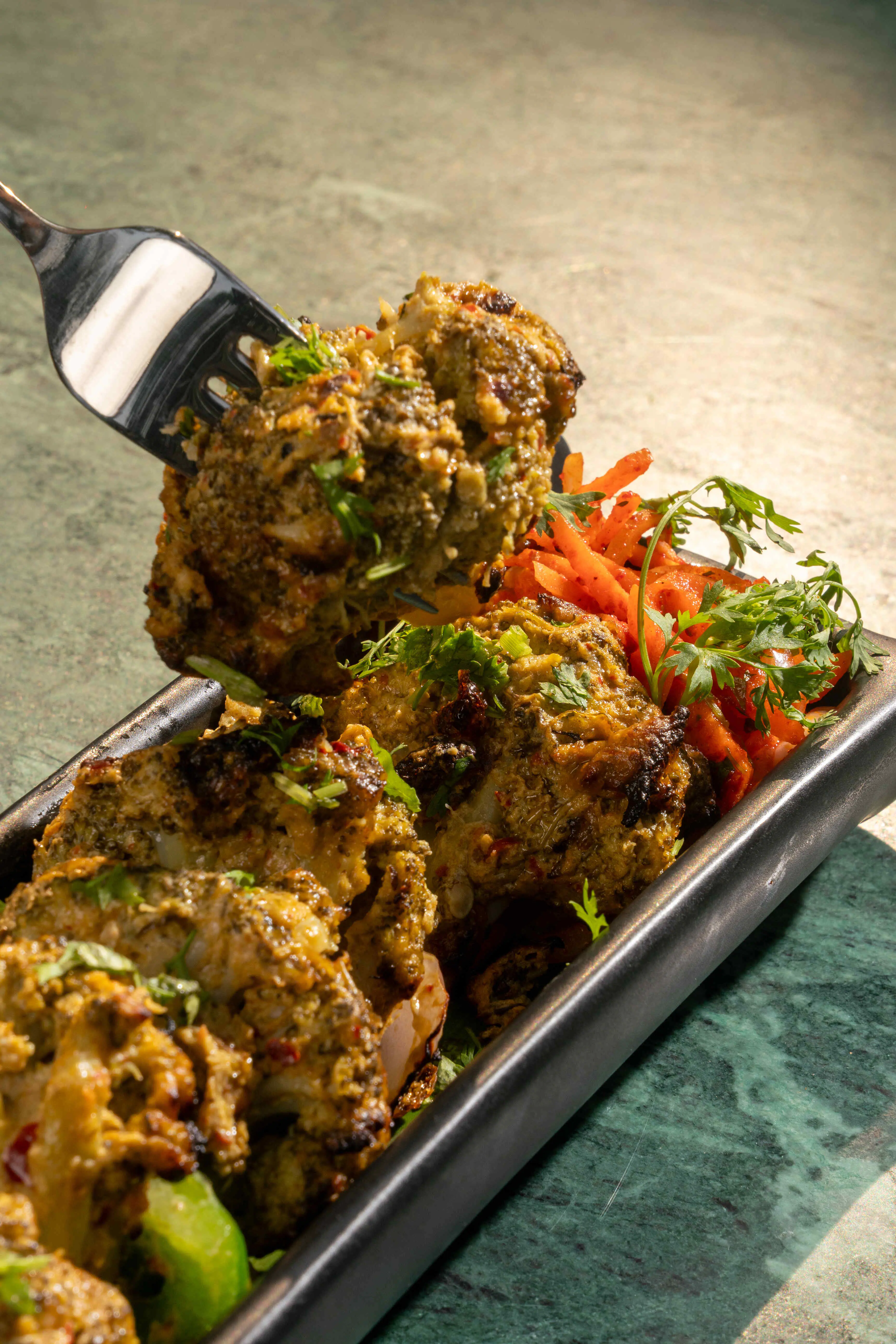 A forkful lifted from a platter of green-marinated kebab.