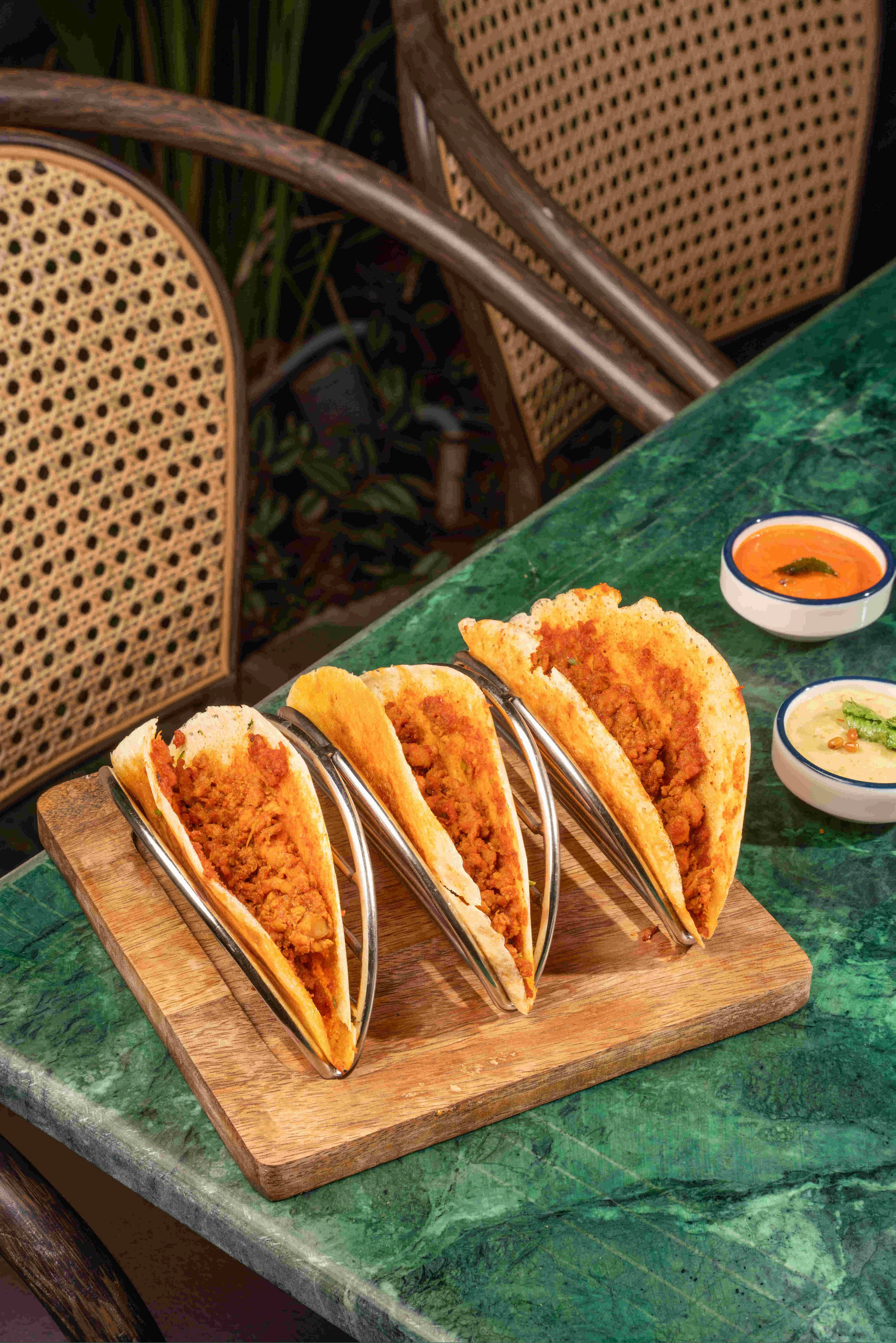 Three folded dosa tacos in a wooden rack with two dips.
