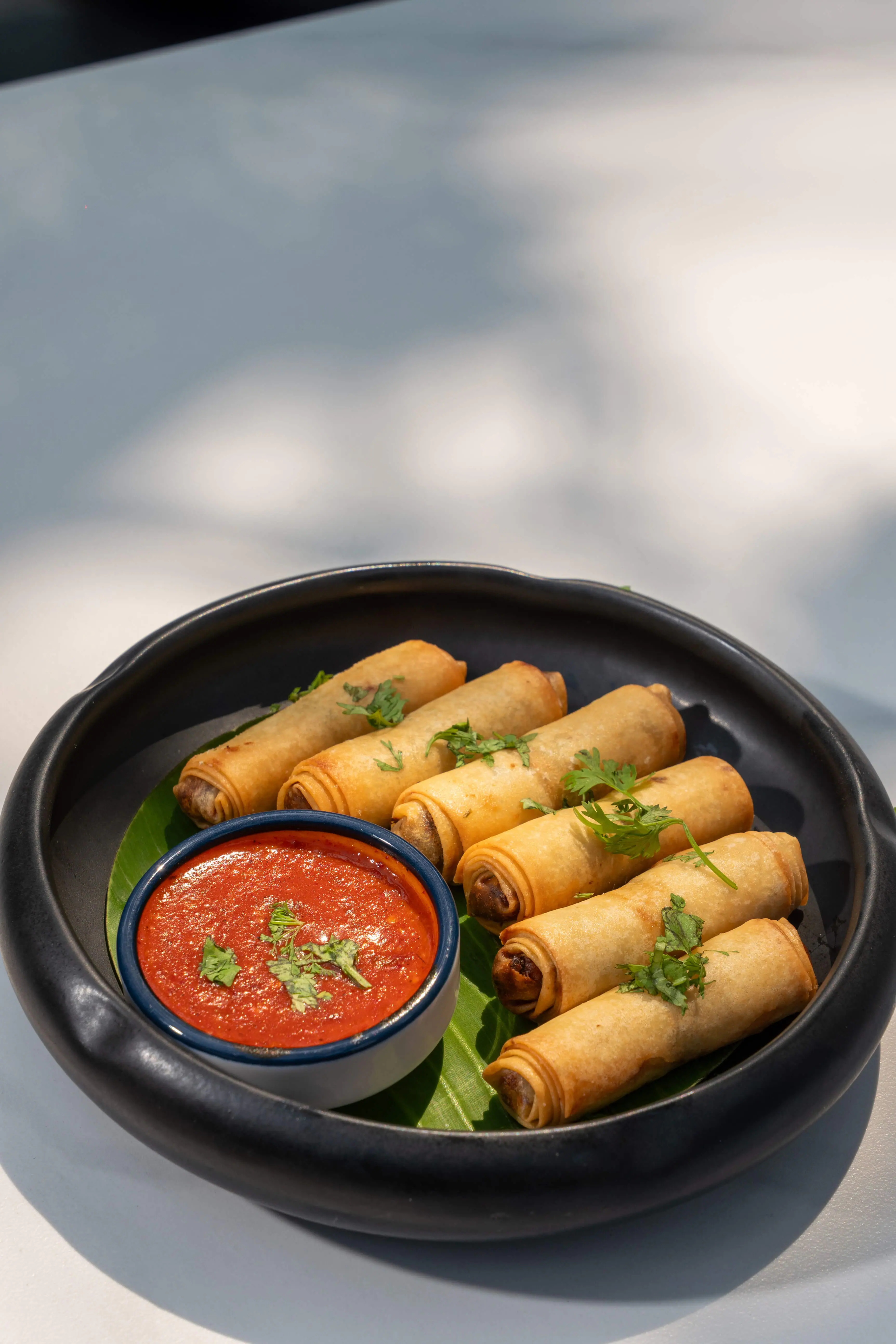 Spring rolls ranged around a red dip in a black bowl.